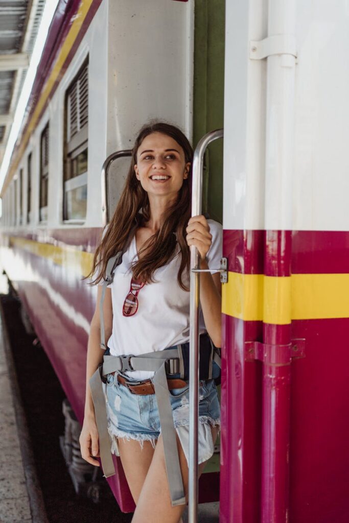 Smiling woman with backpack standing by a colorful train, ready for travel adventure.