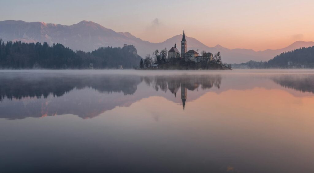 Tranquil morning view of Lake Bled with misty reflections and church silhouette.