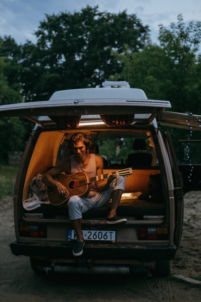 A man enjoys playing guitar in a cozy camper van during a relaxing evening adventure.