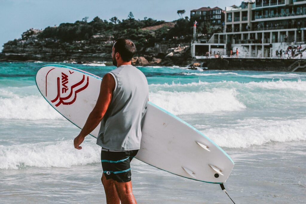 Man holding surfboard on Bondi Beach, Sydney, ready to surf vibrant waves.